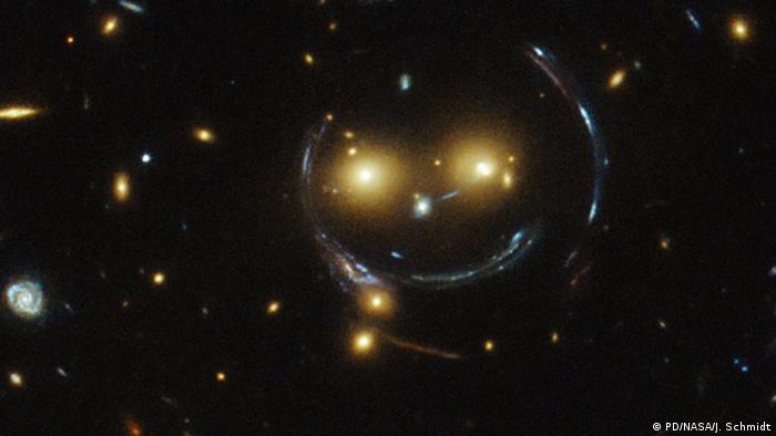 In the centre of this image, taken with the NASA/ESA Hubble Space Telescope, are two faint galaxies that seem to be smiling. You can make out two orange eyes and a white button nose. In the case of this “happy face”, the two eyes are the galaxies SDSSCGB 8842.3 and SDSSCGB 8842.4 and the misleading smile lines are actually arcs caused by an effect known as strong gravitational lensing.