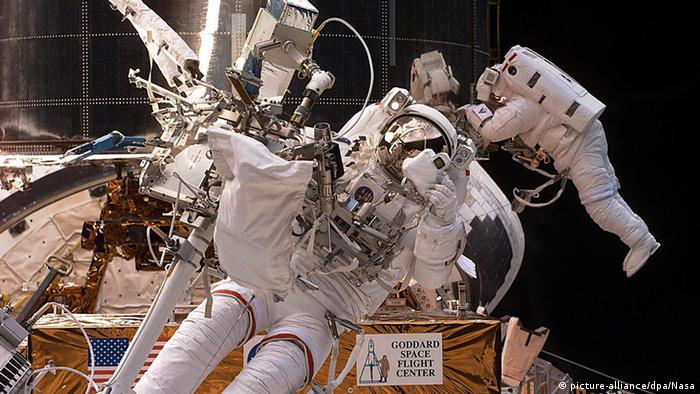 S space shuttle Discovery Mission Specialist Steve Smith of the US (C) prepares to take a photo with a 35mm camera as fellow US Mission Specialist John Grunsfeld (R) moves about the base of the Hubble Space telescope 24 December 1999 during the third and final space walk to service the instrument. 